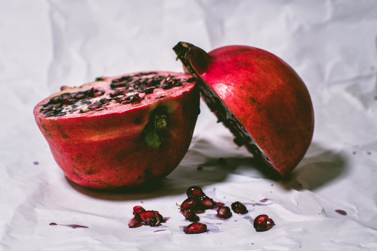 Close-up of fresh pomegranate halves on paper, highlighting vibrant seeds.