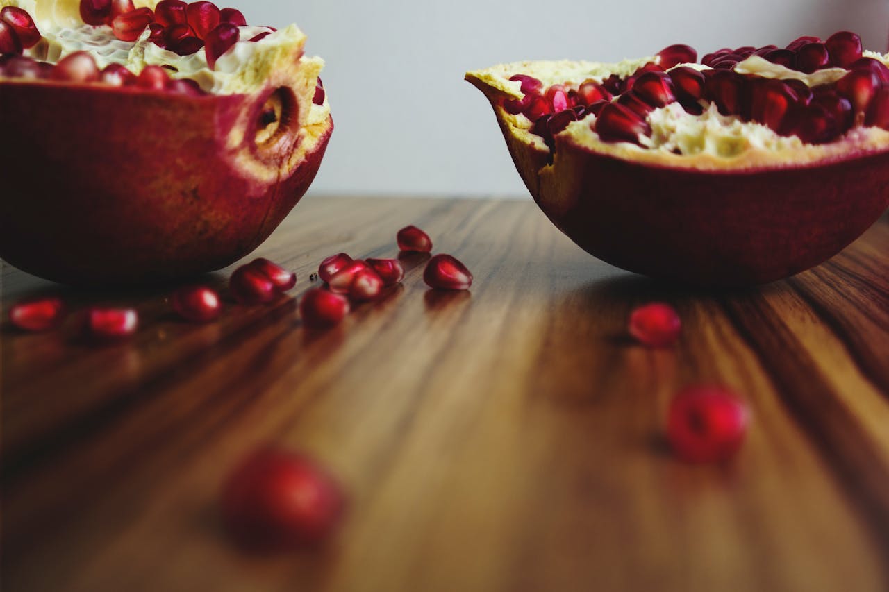 Freshly cut pomegranate with seeds on a wooden table, showcasing vibrant colors.