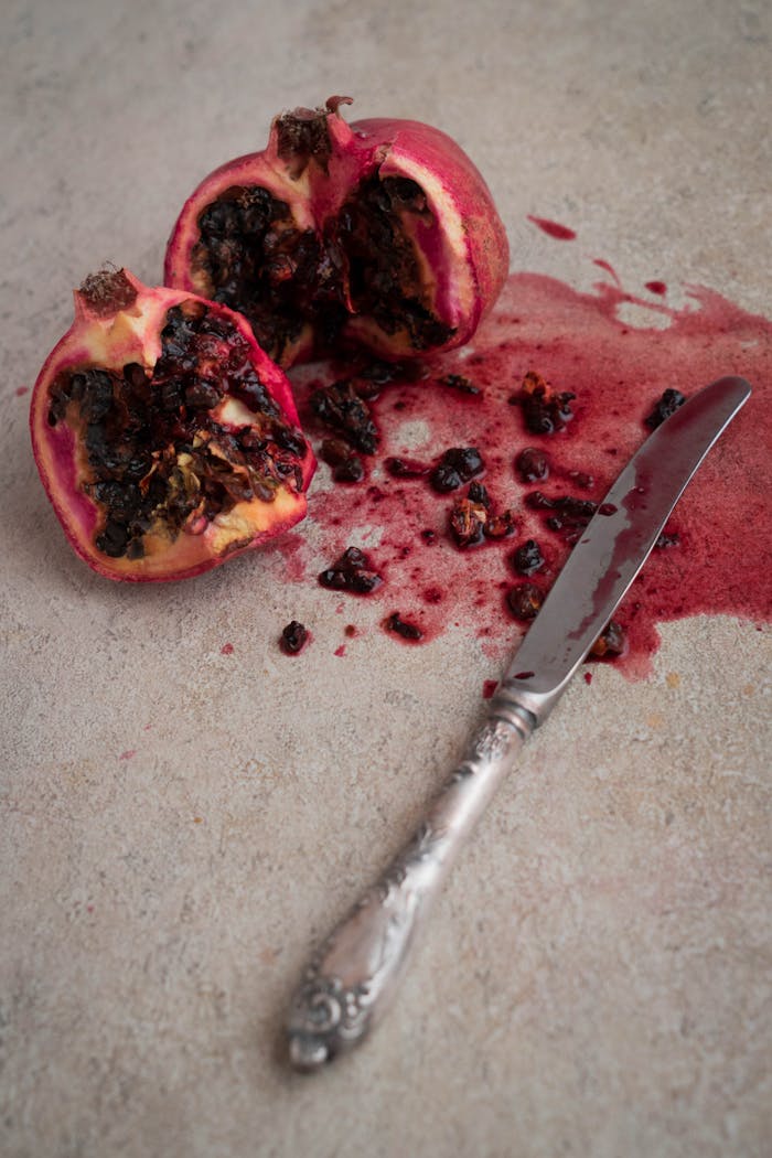 A fresh split pomegranate with a vintage knife on a rustic stone background, highlighting its rich red seeds.