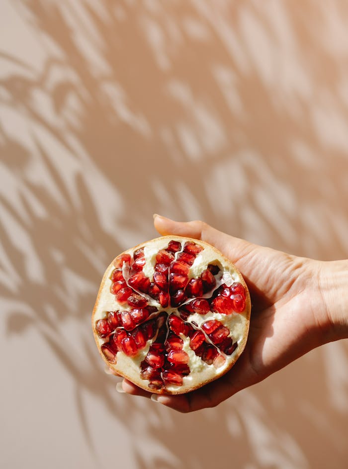 Pomegranate half held against warm shadows, showcasing fresh seeds.
