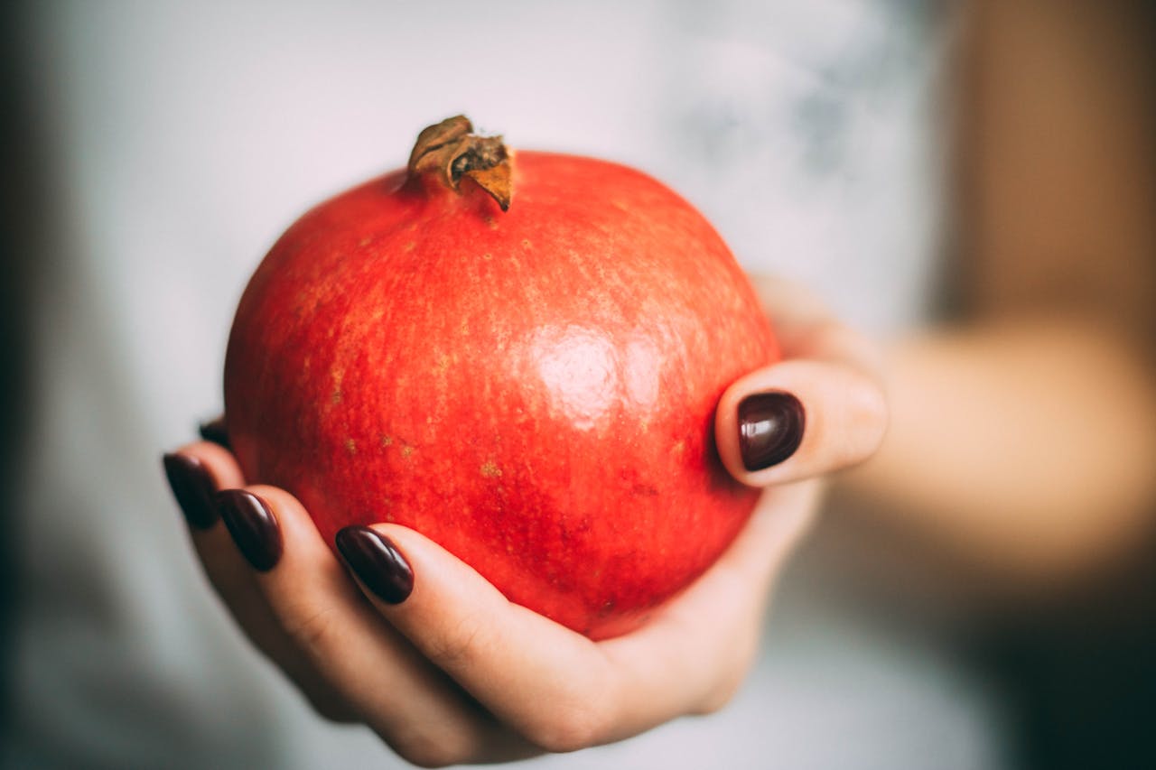 A close-up view of a hand offering a fresh, red pomegranate, symbolizing health and freshness.